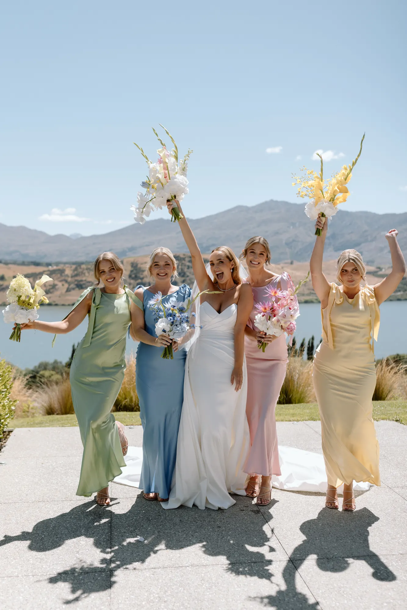 A bride and her bridesmaids cheering with bouquets by the lake