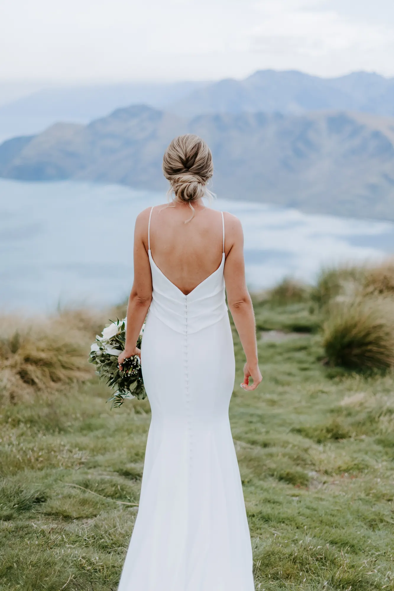 Bride from behind with a twisted low bun above a misty lake